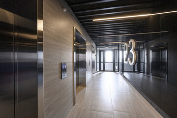 modern hallway features stainless steel elevators, stone walls, and a dark ceiling with linear...