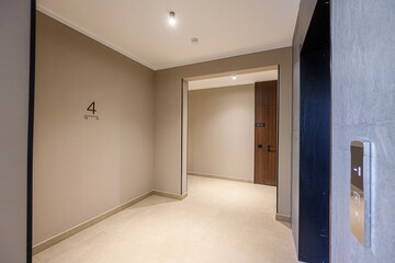 modern apartment corridor with beige walls, light tile flooring, and a view into a hallway. An elevator is visible on the right