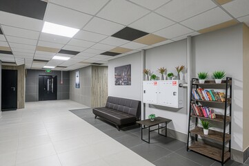 well-lit lobby featuring a sofa, bookshelf, and modern design. Tiles cover the floor and ceiling,...