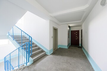 clean, brightly lit entryway features a staircase with blue railings, an elevator, and doors. Walls are mostly white with a light blue accent line