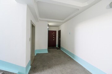 hallway with white walls, a concrete floor, and blue baseboards. There's an elevator, two doors (maroon and dark brown), and the number 