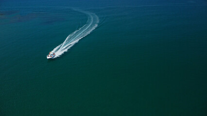 An aerial view captures a powerful speedboat cutting across deep blue water, leaving a dramatic,...