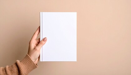A woman's hand gently holds a blank white book against a muted beige background.