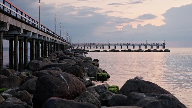 View from the beach to the sea. In the foreground, rocks washed by the water, and in the background, a pier. In Palanga Lithuania