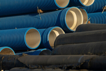 A tall and uneven pile of blue and black pipes is neatly stacked on top of each other, creating an...