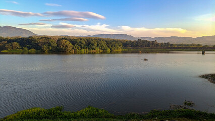 A truly beautiful morning view. The sky is so clear and blue. The reservoir is set against a backdrop of hills and mountains. Someone is fishing in a boat.