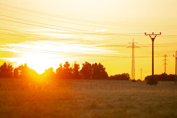 As the sun gracefully sets over a vast field, power lines can be seen prominently in the foreground...