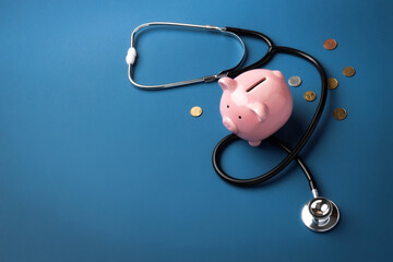 A stethoscope wrapped around a pink piggy bank on a blue background. Healthcare costs, savings and financial aspects of medicine.