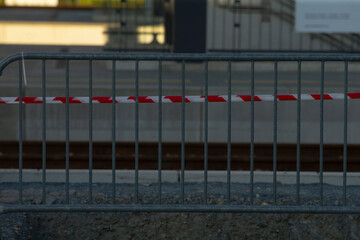 There exists a sturdy metal fence that is adorned with vibrant red and white tape, providing...