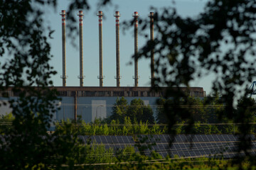A row of tall chimneys can be clearly seen peeking out through the leafy trees that stand in front of the old building