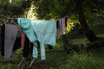 Washed laundry is drying outside under a tree on a drying rack. The sun is shining through the leaves of the tree