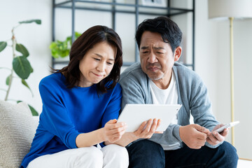 Fototapeta premium リビングでタブレットを見るミドルの夫婦