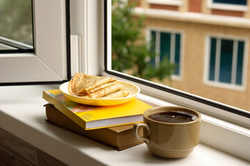Morning coffee and pancakes for breakfast on the balcony. Coffee and pancakes against the background of house windows. Breakfast on the windowsill.