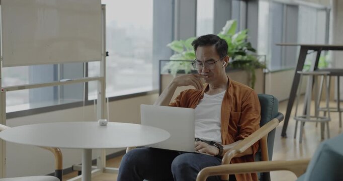 Senior Asian businessman wearing headset celebrates success during online meeting in modern co-working space. Remote work and business communication concept.