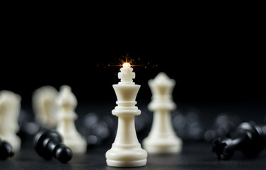 Queen chess piece stands among fallen silver knights, rooks, bishops and pawns on a chessboard....