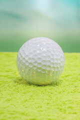 A golf ball resting on a bright green textured surface. The soft, blurry background draws attention...