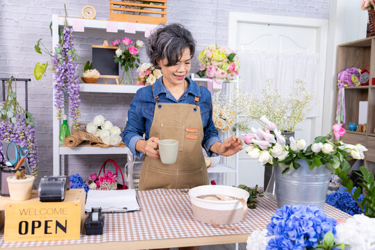 Small business, florist, flower, lifestyle, senior Asian woman taking break with coffee in hand, healthy elderly retirement enjoying working moment during silver-age career journey, occupation passion