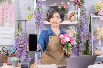 Asian senior woman, florist, small business, owner holding bouquet and smartphone in flower shop, presenting service, digital marketing confidence, and floral, modern aging people with technology