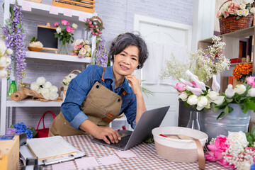 Florist small business senior woman lifestyle holding credit card and laptop, florist Asian female presenting contactless payment, confident silver-age retail owner modern aging people with technology