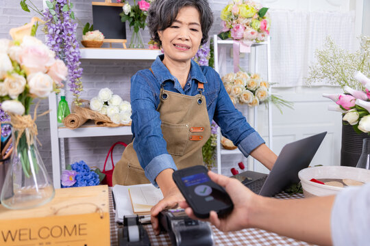 Asian senior woman, small business lifestyle florist shop accepts credit card payment cashless, smile elderly flower entrepreneur handling retail transaction, modern aging people with technology - Powered by Adobe