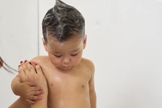 1 year old baby being bathed by mother, soap, water running over body, minimalist background with white background and bathtub