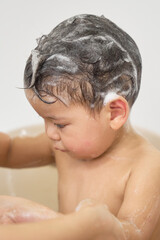 1 year old baby being bathed by mother, soap, water running over body, minimalist background with...