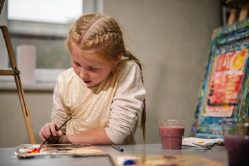 Child draw a picture in art class. Girl enjoys painting in a workshop. Art lesson. Education and...