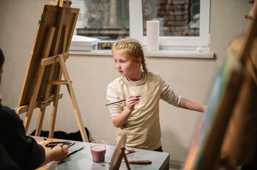 Child draw a picture in art class. Girl enjoys painting in a workshop. Art lesson. Education and...