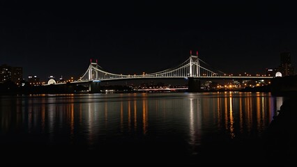 Obraz premium A majestic suspension bridge illuminated at night, reflects golden lights on the water below.