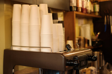 Close-up of coffee shop espresso machine with neatly stacked white disposable cups and black lid...
