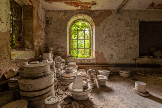Abandoned pottery molds stacked in a decaying workshop with peeling walls and a bright green window view, showcasing forgotten craftsmanship and urban decay