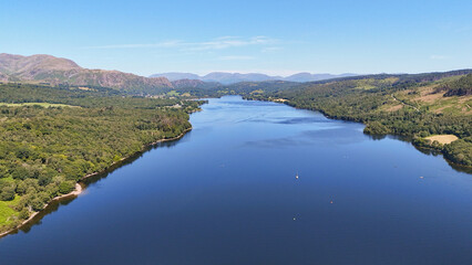 Sweeping drone view of Lake Coniston surrounded by hills and forests on a clear summer day