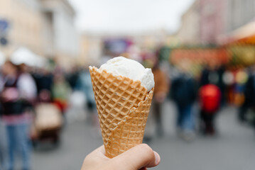 white ice cream cone in hand, waffle cone, pov, blurred crowd in background