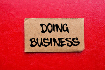 Doing business message written on ripped torn cardboard paper piece on red background. Conceptual...