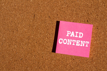 Paid content message written on pink paper sticker on brown background. Conceptual paid content...