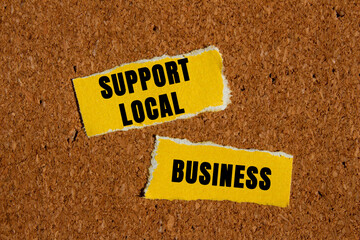 Support local business message written on ripped torn yellow paper pieces on brown background....