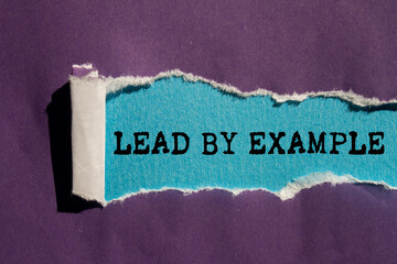 Lead by example message written on ripped torn purple paper on blue background. Conceptual lead by...