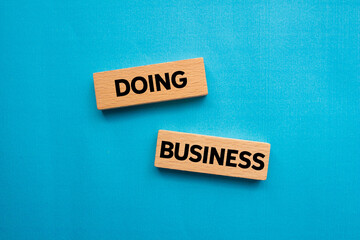 Doing business message written on wooden blocks on blue background. Conceptual doing business...