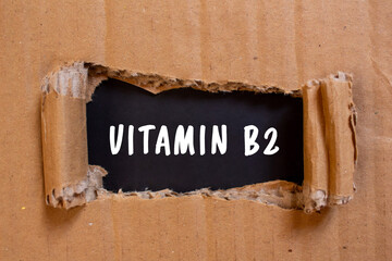 Vitamin B2 message written on ripped torn cardboard paper on black background. Conceptual Vitamin...