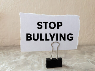 Stop bullying message written on ripped torn white paper piece on wall background. Conceptual stop bullying symbol. Copy space.