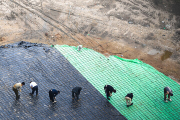 Aerial view of multiple construction workers installing a steel rebar grid over a foundation at a...
