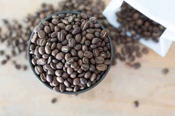 Dark bowl overflows with aromatic, freshly roasted coffee beans on wood table