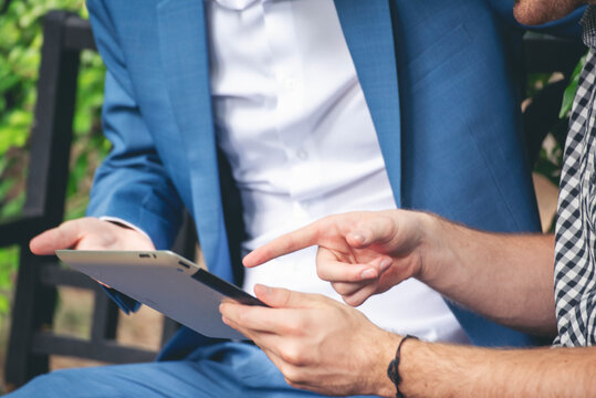 Close up Two Businessman caucasian hands using smartphone digital tablet discussion sitting wood table green garden. Two Man hands hoding touch screen smart phone surf internet relax in green park