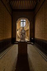 Naklejka premium Historic statue illuminated by natural light in an abandoned French chateau with a spiral staircase in the background