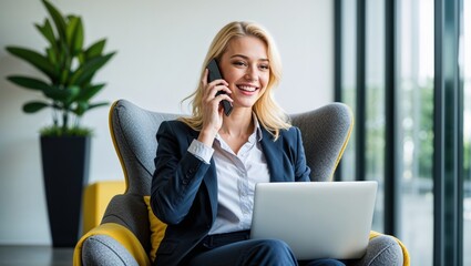 Happy young blonde businesswoman talking on a smartphone and working on a laptop in a modern office lounge.
