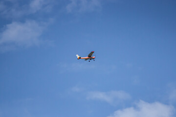 Small White and Orange Airplane Flying High in the Bright Blue Sky