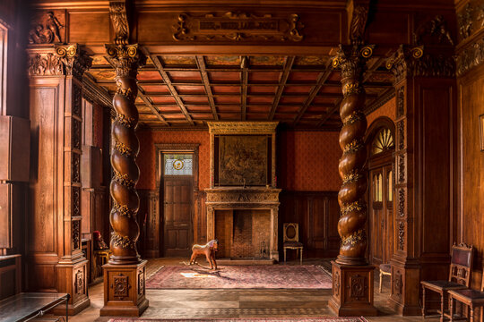 Ornate abandoned mansion interior with carved wooden columns, vintage fireplace, antique rocking horse and classic furniture in warm natural light