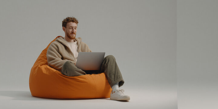 A man working on a laptop while sitting on an orange beanbag chair