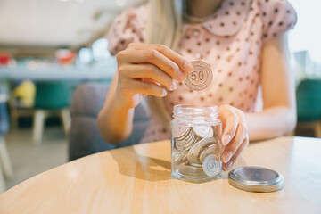 Saving money concept. Female Hand Adding Coins to Glass Jar on Wooden Table