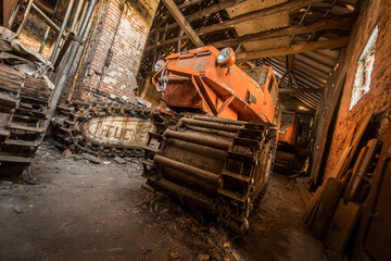 Fototapeta premium Rusty vintage tracked vehicle in abandoned barn with decayed brick walls and wooden beams